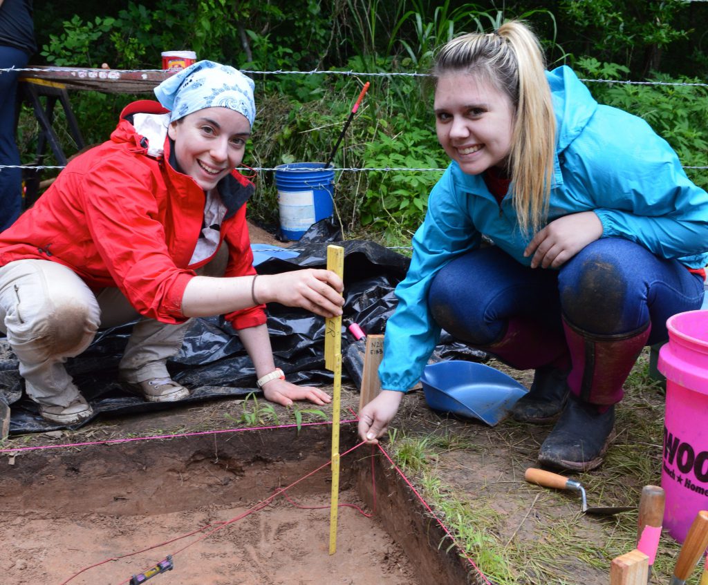 Two women next to an excavation unit