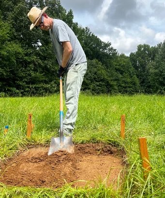 A man digs a square hole in the ground. Showing the practice of archeological excavation.