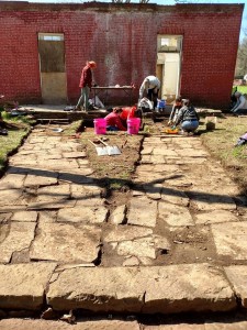 Crew cleaning the stone walkways at the Methodist Manse at Cane Hill during the 2015 Spring Break Dig.