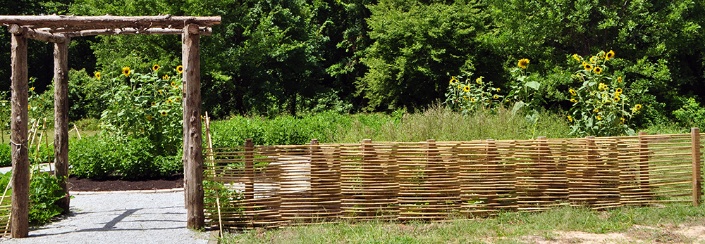 A view of the entrance and woven fence surrounding the Plum Bayou Garden