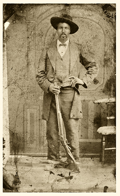 A sepia-toned photograph of an African-American man wearing a hat and posing with a long gun.