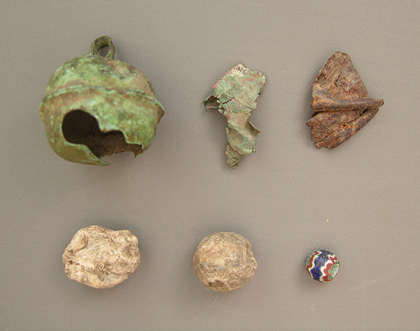 Early sixteenth-century Spanish artifacts from the Parkin site. Top (l to r): Clarksdale bell of brass; Clarksdale bell fragment of brass; possible Clarksdale bell fragment of bronze. Bottom (l to r): lead shot that was fired or damaged; unfired lead shot (.61 caliber); seven-layer faceted chevron bead. ARAS photo.