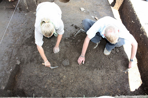  Photo of two field archeologists using trowels in an excavation unit.