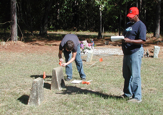 Two men standing in a cemetery documenting information from gravestones.