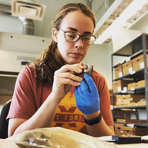 Photo of Toltec station archeologist Paige Ford analyzing an artifact in a lab.