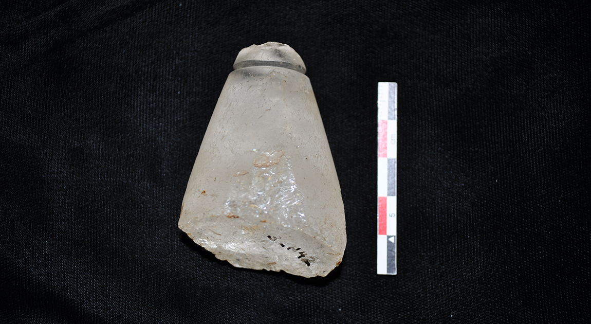 Photo of a prehistoric quartz crystal plummet next to a measurement scale.