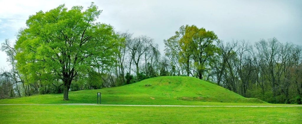 Landscape view of a large earthen mound surrounded by trees on an overcast spring day