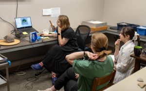 A woman using a laptop while two others watch.